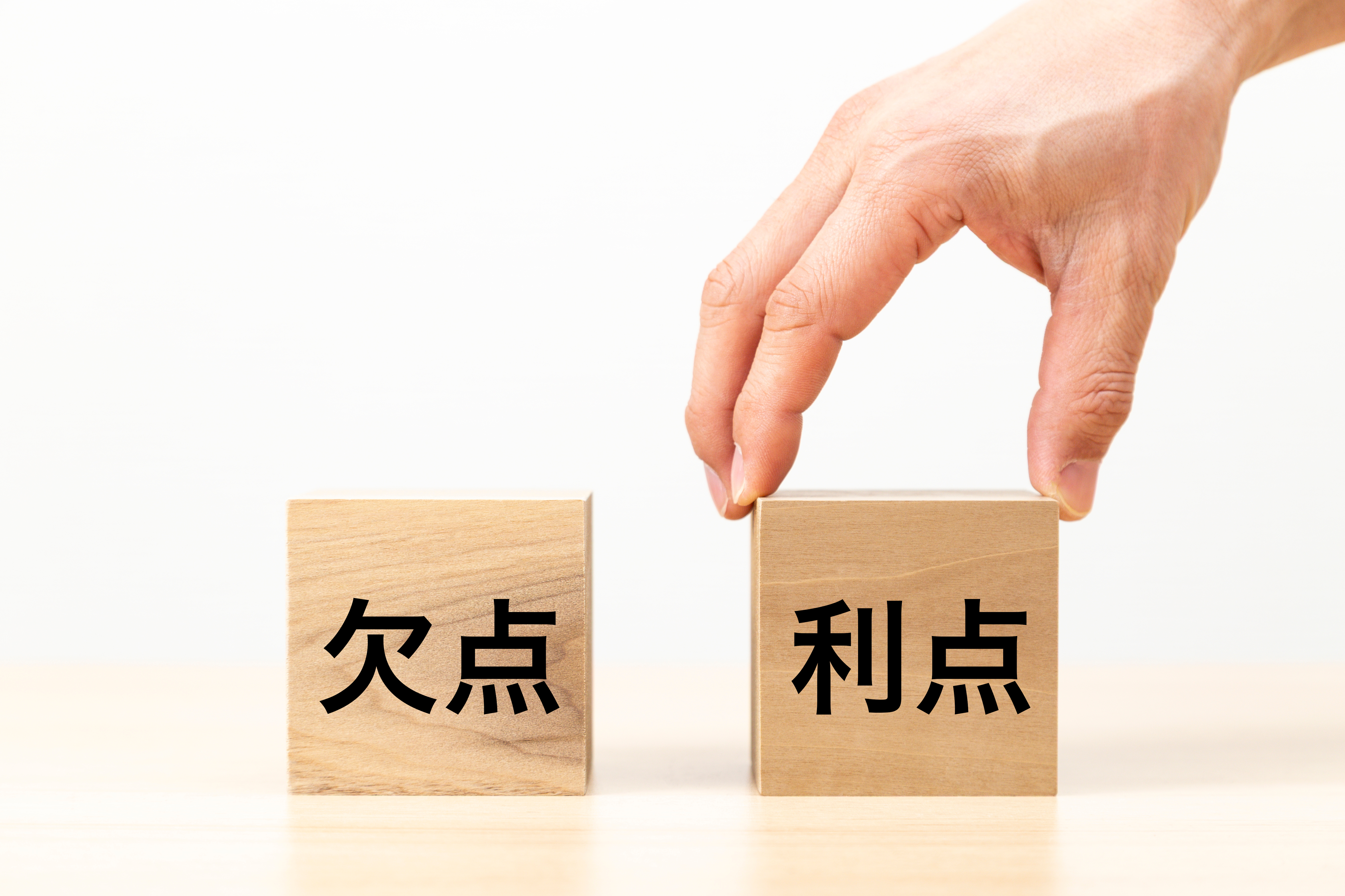 「欠点」と「利点」と書かれた木製ブロックが並び、そのうち「利点」のブロックに手が添えられているメリット・デメリットの比較イメージ